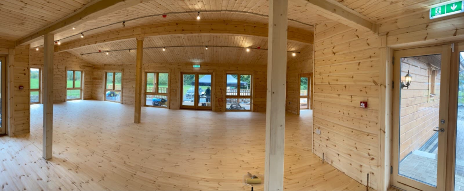 Empty timber hall with exposed posts, ceiling boards and glazed doors.